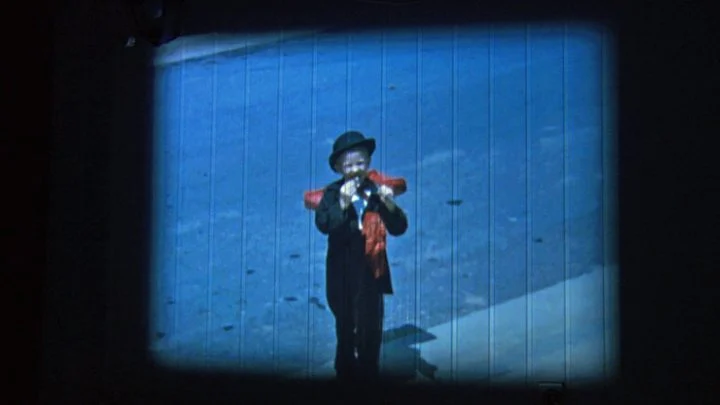 A figure stands against a blue background in a projected image from Poem of Death.